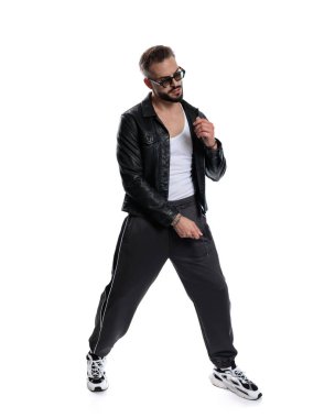 Güneş gözlüklü seksi sakallı adam beyaz arka planda aşağı bakarken havalı bir poz veriyor.