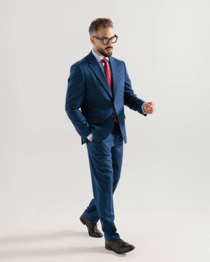 Donanma mavisi takımlı zarif genç adam gözlerini kaçırıyor ve gri arka planda el ele yürüyor.