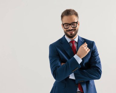 Lacivert takımlı mutlu iş adamı kollarını kavuşturup gri arka planda gülümserken gözlerini kapatıyor.