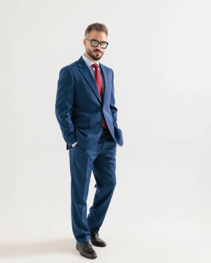 Lacivert takım elbiseli zarif bir iş adamı elleri ceplerinde gri arka planda yürüyor.