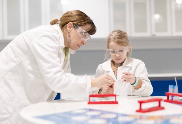 Young student works girl in laboratory with help of teacher in school