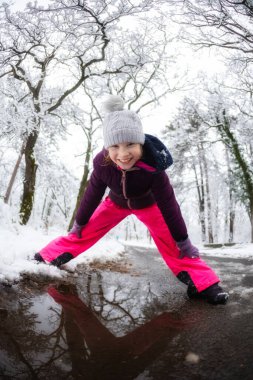 Kışın kar ormanında gülümseyen neşeli kız çocuğu.