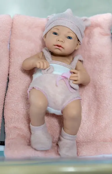 かわいい赤ん坊の人形はピンクの毛布に横たわっています ロイヤリティフリーのストック画像