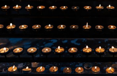 Karanlık kilisede dizilmiş parlak mumlar.