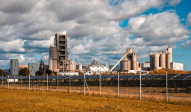 Ön planda güneş panelleri olan çimento fabrikası