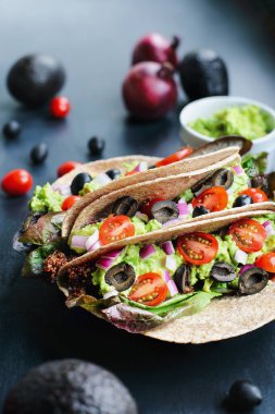 Tako sezonlu kırmızı kinoalı, romaine marullu, dilimlenmiş domatesli, guacamole, siyah zeytinli ve kırmızı soğanlı vegan / vejetaryen yumuşak kabuklu taco dürümünden oluşan sağlıklı bir öğle veya akşam yemeği. Seçici odak.