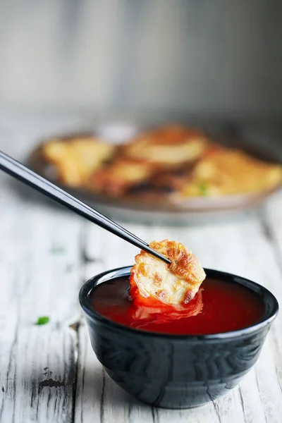 筷子在一碗红糖酸酱汁中蘸入金黄色的中国饺子 也被称为肉片 背景模糊的选择性重点 — 图库照片