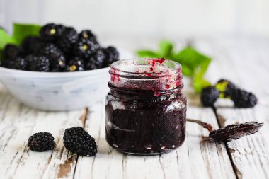 Homemade blackberry preserves or jam in a mason jar surrounded by fresh organic blackberries. Selective focus with blurred foreground and background.