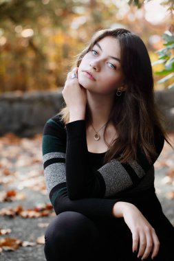 Güzel, esmer, genç bir kadın. Etrafı sonbahar renkleriyle çevrili kameraya dikkatlice bakıyor. Bulanık arkaplan ile seçmeli odak.