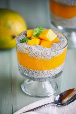 Yeşil ahşap arka planda cam bir kavanozda taze nane şekerli nefis vegan mango chia pudingi. Önplanı ve arkaplanı bulanık seçili odak.