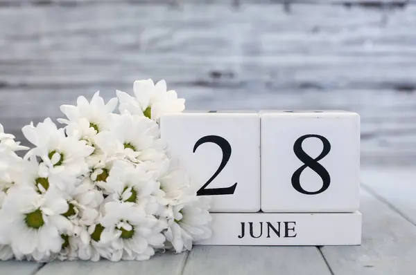 ホワイトウッドのカレンダーブロックは 6月28日とホワイトデイジーの日付です バックグラウンドで選択的なフォーカス ストック画像
