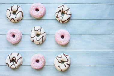 Çikolata kıvrımlı buzlu vanilyalı çörek ve hindistancevizi gevrekli pembe çörekler. Masa üstü manzarası. Düz arkaplan.