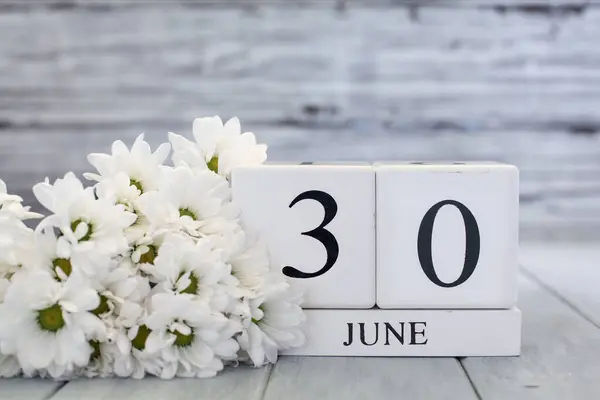 日期为6月30日的白色木制日历块和白色雏菊 背景模糊的选择性重点 免版税图库照片