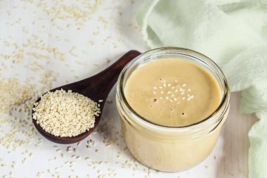 Tahini dolu mason kavanozunun en üst görüntüsü. Tahta kaşık susam tohumlarıyla dolup taşıyor. Üst görünüm. 