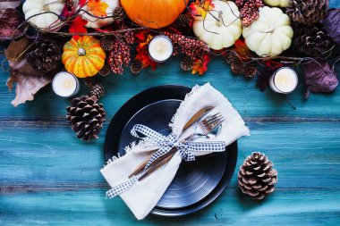 Düz bir tabakta, gümüşleri ve peçetesi olan düz bir tabakta sonbahar çelengi olan ahşap bir masanın üzerine kurulmuş.. 