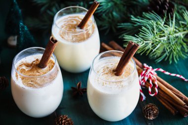 Tarçın çubuklu üç bardak kremalı eggnog ve anason yıldızı. Bulanık şenlik arkaplanlı seçici odak.