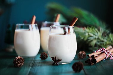 Tarçın çubuklu üç bardak kremalı eggnog ve anason yıldızı. Bulanık şenlik arkaplanlı seçici odak.