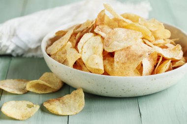 Parlak bir masanın üzerinde kasede çıtır patates cipsi. Bulanık arkaplan ile seçmeli odak.