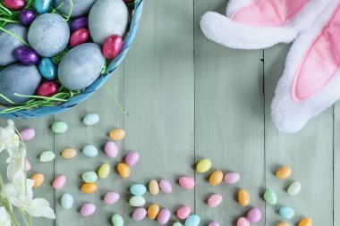 Doğal olarak boyanmış mavi Paskalya yumurtaları, arka planda şeker ve tavşan kulakları olan bir sepette. Bulanık arkaplan ile seçmeli odak.