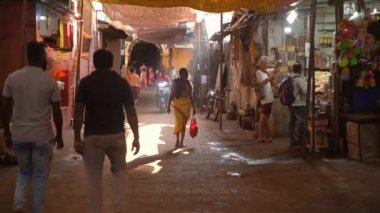 Gokarna, Hindistan - 21 Şubat 2023 - Gokarna 'da sabah, insanlar gün ışığıyla aydınlanmış bir cadde boyunca yürüyorlar. Geleneksel Shaivite turuncu elbiseli adam scooter kullanıyor..