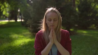 Güneş ışığında meditasyon yapan genç bir kadın. Gözleri kapalı, elleri dua pozisyonunda, ağır çekimde..