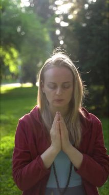 Güneş ışığında meditasyon yapan genç bir kadın. Gözleri kapalı, elleri dua pozisyonunda, ağır çekimde..