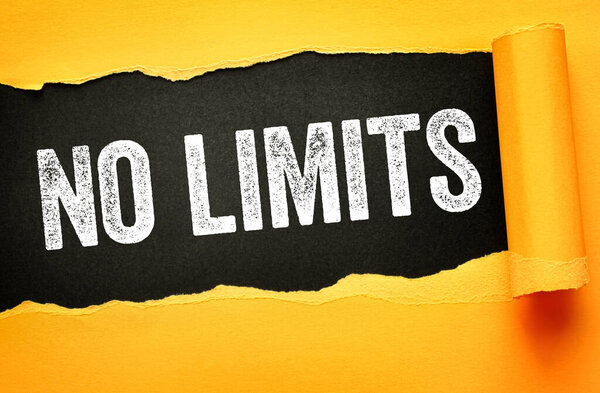 НЕОГРАНИЧЕННЫЙ текст, показанный через порванную желтую бумагу на чёрном фоне. Мотивационная концепция, символизирующая свободу, расширение прав и возможностей, амбиции, возможность и личностный рост