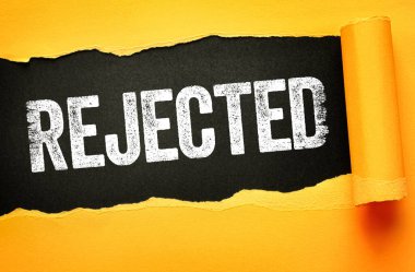 Koyu, sıkıntılı beyaz yazı tipiyle yazılmış olan REJECTED metni siyah arka plandaki yırtık sarı kağıdın altında ortaya çıktı. İnkar, başarısızlık, onaylama, reddedilme ve olumsuz karar kavramı