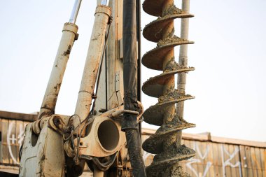 Toprakla kaplanmış, toprak kazmak veya kazmak için kullanılan bir endüstriyel sondaj makinesinin yakın çekimi. Ağır makineler, inşaat gücü ve mühendislik operasyonlarını vurgular