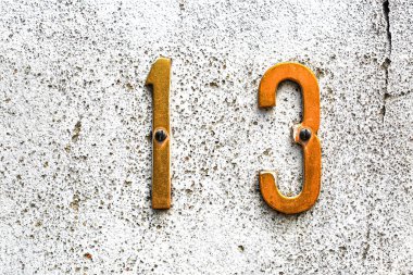 Pürüzsüz, beyaz bir duvar üzerine monte edilmiş 13 numaralı altın metal evin yakın çekimi. Eski rakamlar ve görünür vidalar mimari ya da tasarım temalı görseller için mükemmel bir klasik görünüm yaratıyor.
