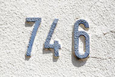 746 numaralı yıpranmış mavi ev desenli beyaz bir duvara monte edilmiş. Boyalı rakamlar aşınma ve yaşlanma belirtileri gösteriyor, kırsal, klasik estetik mimari ve tasarım temalarını çağrıştırıyor.