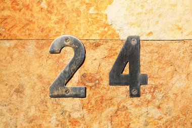 24 numaralı metal ev güneş ışığıyla döşenmiş taş duvara vidalarla sabitlenmiş. Köy arka planında modern metalik rakamlar, adres, kimlik, mülk ve sokak işaretleme kavramı