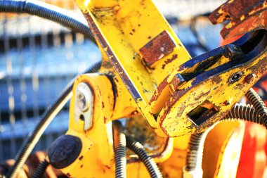 Paslı, cıvatalı ve çelik hortumlu yıpranmış sarı bir hidrolik makine parçasına yakın çekim. Endüstriyel yapı, ağır mühendislik, inşaat gücü ve mekanik hassasiyeti vurguluyor