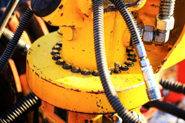 Civata, hortum ve konnektörlü sarı endüstriyel hidrolik makine parçasına yakın çekim. Yıpranmış metal yüzeylerin detaylı dokusu mühendislik, mekanik ve ağır ekipman kullanımını vurgular