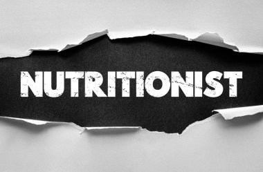 Yırtık kağıdın altında ortaya çıkan, kederli ve kalın harflerle yazılmış NUTRITIONIST kelimesi. Sağlık, dengeli beslenme, diyet planlaması, refah rehberliği ve profesyonel beslenme hizmetleri kavramı