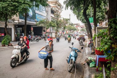 Hanoi, Vietnam, 13 Kasım 2022: Bir sepet sebze taşıyan yaşlı bir kadın, Hanoi, Vietnam 'da işlek bir ara sokaktan geçerken scooter trafiğine yön veriyor