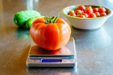 Mutfak masasının üzerinde, arka planda bir kase salatalık ve domates olan büyük bir biftek domatesi.