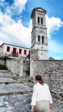 Yunanistan 'ın Arcadia bölgesindeki Karitaina köyünde saat kulesine doğru yürüyen bir kadını gösteren dikey video klip