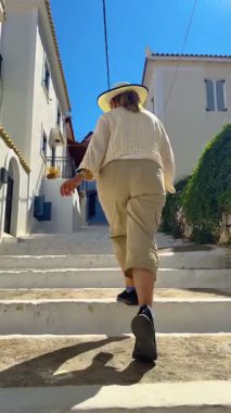 Yunanistan 'ın Mora eyaletinin Koroni kasabasında bir yayanın merdivenlerinde yürüyen bir kadının dikey video klibi