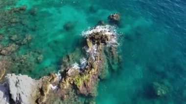 Dalgaların mavi okyanustaki Alanya Hindi kıyısındaki kayalıklardaki uçurumlara düşüşünü gösteren hava manzarası. Yeşil doğa ve okyanusun hava aracı fotoğrafçılığı