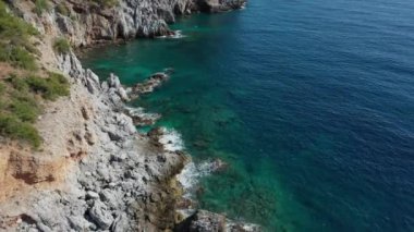 Dalgaların mavi okyanustaki Alanya Hindi kıyısındaki kayalıklardaki uçurumlara düşüşünü gösteren hava manzarası. Yeşil doğa ve okyanusun hava aracı fotoğrafçılığı