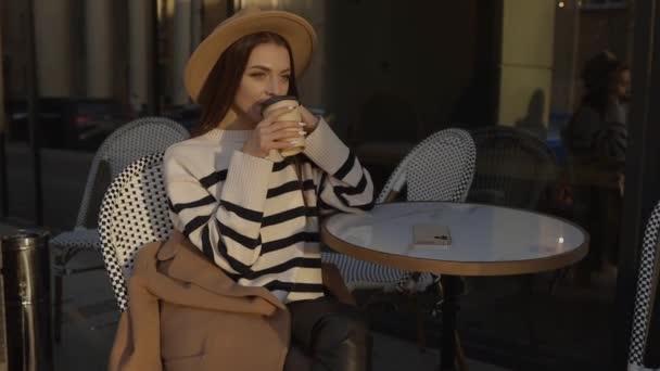 Piękna Młoda Dziewczyna Kapeluszu Siedząca Ulicznej Kawiarni Odwracając Wzrok Pijąc — Wideo stockowe