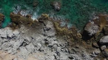Dalgaların mavi okyanustaki Alanya Hindi kıyısındaki kayalıklardaki uçurumlara düşüşünü gösteren hava manzarası. Yeşil doğa ve okyanusun hava aracı fotoğrafçılığı