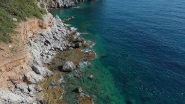 Dalgaların mavi okyanustaki Alanya Hindi kıyısındaki kayalıklardaki uçurumlara düşüşünü gösteren hava manzarası. Yeşil doğa ve okyanusun hava aracı fotoğrafçılığı