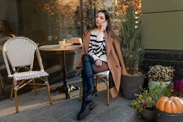 在欧洲一个城市的街道上散步时 一位穿着休闲装的黑发美女坐在咖啡店里 与人通电话 — 图库照片