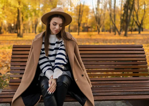 공원에서 머리를 코트를 유행하는 스타일의 모자를 매력적 미소짓는 여성의 — 스톡 사진