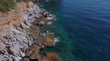 Dalgaların mavi okyanustaki Alanya Hindi kıyısındaki kayalıklardaki uçurumlara düşüşünü gösteren hava manzarası. Yeşil doğa ve okyanusun hava aracı fotoğrafçılığı