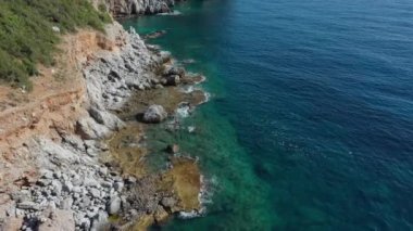 Dalgaların mavi okyanustaki Alanya Hindi kıyısındaki kayalıklardaki uçurumlara düşüşünü gösteren hava manzarası. Yeşil doğa ve okyanusun hava aracı fotoğrafçılığı