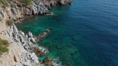 Dalgaların mavi okyanustaki Alanya Hindi kıyısındaki kayalıklardaki uçurumlara düşüşünü gösteren hava manzarası. Yeşil doğa ve okyanusun hava aracı fotoğrafçılığı