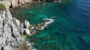 Dalgaların mavi okyanustaki Alanya Hindi kıyısındaki kayalıklardaki uçurumlara düşüşünü gösteren hava manzarası. Yeşil doğa ve okyanusun hava aracı fotoğrafçılığı